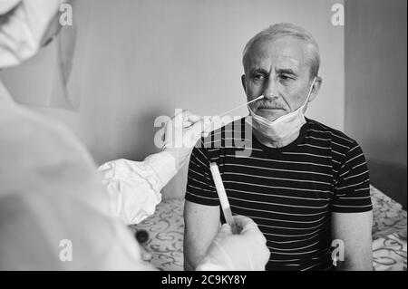 Fotografia in bianco e nero della visita del medico a casa. Infermiere che prende l'analisi del test del coronavirus con tampone medico a pazienti anziani di sesso maschile. Provetta per il prelievo del campione paziente OP NP. Foto Stock