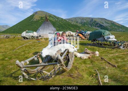 YAMAL, RUSSIA - 27 AGOSTO 2018: Ragazzino e bambina sulle slitte nel campo dei moderni pastori di renna in una giornata estiva di sole Foto Stock