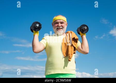 Sportivo anziano che si esercita con sollevamento dumbell su sfondo cielo blu. Spazio di copia isolato. Foto Stock