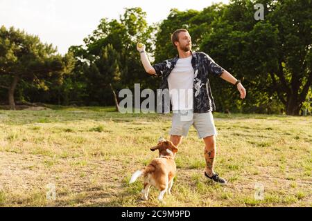 Immagine del giovane uomo caucasico bearded che gioca con il suo cane beagle mentre cammina nel parco estivo Foto Stock