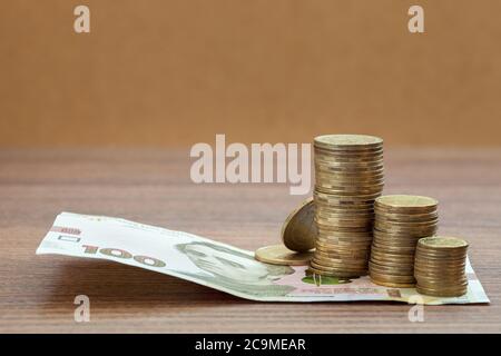 Un mucchio di monete in colonne giacciono su un centinaio di hryvnia giace su un tavolo di legno. Foto Stock