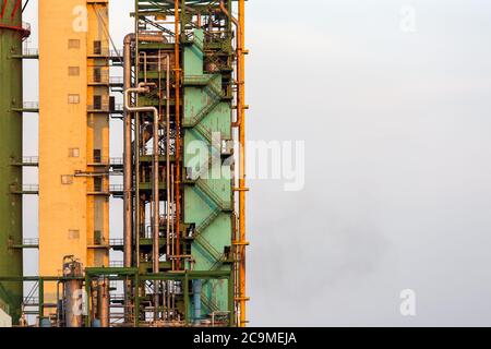 Un primo piano di un alto edificio industriale di un impianto di ammoniaca, una torre con tubi e una scala per la manutenzione contro il cielo con spazio di copia per il testo. Foto Stock
