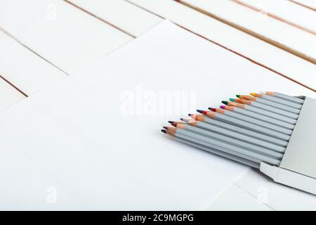 diverse matite colorate che stanno guardando fuori da un pacco che sono sul foglio di carta che giace su un tavolo di legno dalla lavagna bianca. Foto Stock