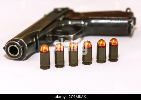 Sei cartucce di pistole da combattimento di calibero da 9 mm si trovano di fronte a una pistola su sfondo bianco vista laterale, armamento e concetto di armi, selettivi Foto Stock