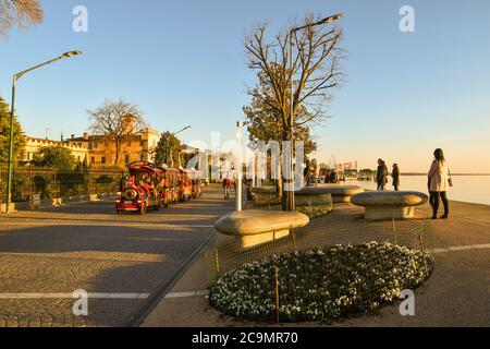 Trenino turistico che corre lungo il lungolago della cittadina sulle sponde del Lago di Garda in inverno al tramonto, Bardolino, Verona, Veneto, Italia Foto Stock