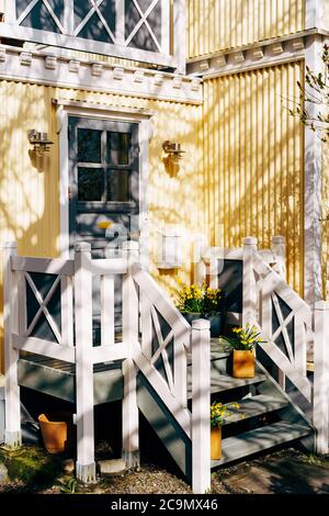 Una porta con vetro in un edificio giallo corrugato con corrimano bianchi e scalini decorati con vasi di fiori. Foto Stock