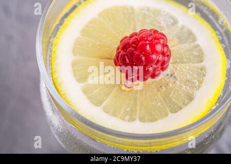 Bevanda fresca fredda con limone, frutta lampone in vetro su fondo di pietra in cemento, bevanda estiva dieta, macro angle view Foto Stock