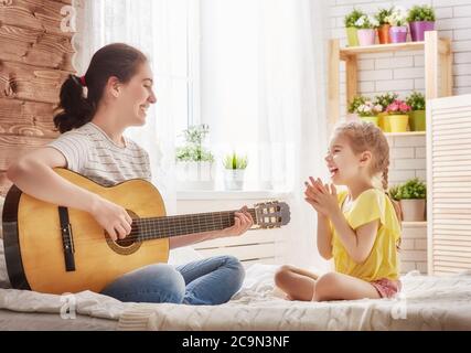 Buona famiglia. Madre e figlia suonano insieme la chitarra. Donna adulta che suona la chitarra per bambina. Foto Stock