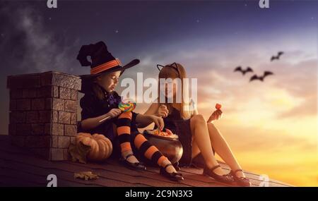 Due sorelle felici su Halloween. Bambini divertenti in costumi di carnevale  seduti sul tetto. Bambini allegri con zucca, bacchetta magica e libro di  incantesimi Foto stock - Alamy