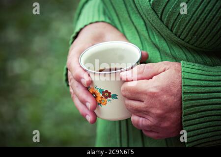 Primo piano delle mani della donna anziana, tenendo una tazza di caffè in metallo, all'aperto. Foto Stock