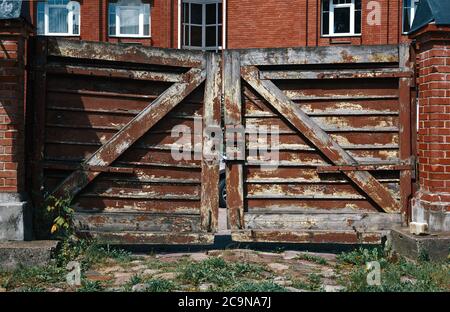 Cancelli di legno di shabby con una serratura vicino casa di campagna di mattoni Foto Stock