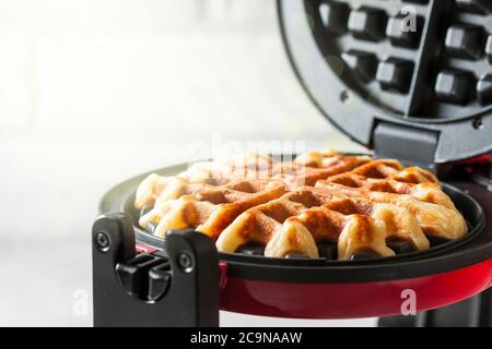 Il processo di preparazione di waffle fatti in casa. Waffle appena sfornati in un ferro da stiro a base di waffle. Messa a fuoco selettiva Foto Stock