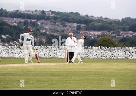 Bowler che corre oltre l'umpire a ciotola ad una partita di cricket del villaggio nello Yorkshire occidentale Regno Unito Foto Stock