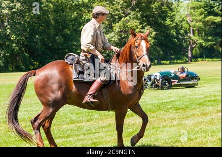 Un uomo che cavalca un cavallo in primo piano e un uomo che guida un Morgan 3-Wheeler in background all'evento Race of the Century presso la Collings Foundation. Foto Stock