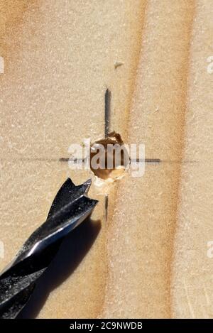 Un ritratto closeup di una tavola di legno con un foro trapanato in essa sull'intersezione delle linee di una marcatura a matita con la punta di foratura del legno giacente Foto Stock