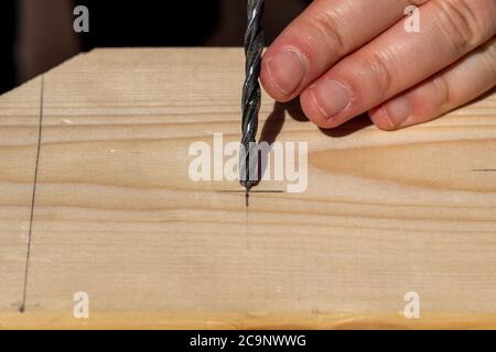 Un ritratto closeup di qualcuno che mira e il posizionamento della punta di una punta da trapano di legno alla matita tracciata contrassegno fatto su una tavola di legno per iniziare a forare un ho Foto Stock