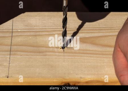 Un ritratto in primo piano di una persona che perfora un foro in una tavola di legno sulla marcatura disegnata a matita. La punta per legno è già una punta all'interno del pezzo Foto Stock