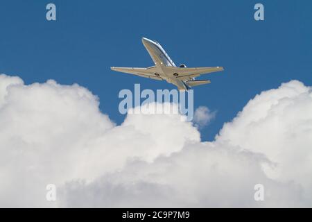 Un jet aziendale vola sopra nuvole bianche e soffici in un cielo blu profondo. Foto Stock