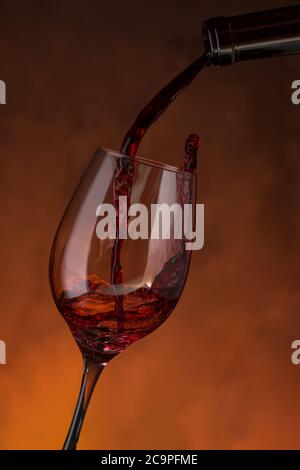 Bottiglia che riempie un bicchiere di vino rosso su fondo rossastro Foto Stock