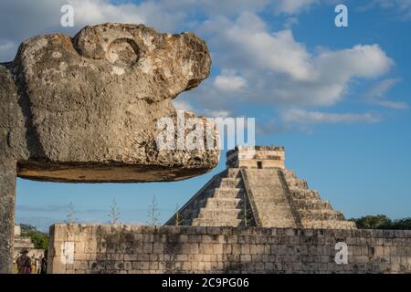 Una testa di pietra scolpita giaguaro al campo da ballo grande nelle rovine della grande città maya di Chichen Itza, Messico. Dietro si trova il Castello o El Castillo. Foto Stock