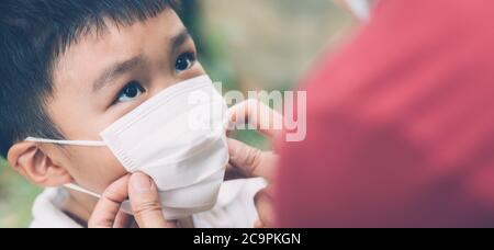 Madre prendersi cura figlio con maschera viso per la protezione malattia influenza o covid-19 all'aperto, mamma indossare su maschera medica con sicurezza del bambino per proteggere l'esterno Foto Stock