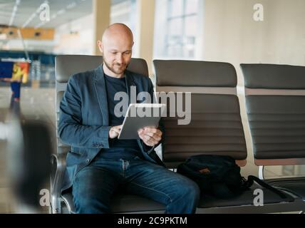 Bell'uomo d'affari calvo adulto in tuta usando un tablet nella lounge dell'aeroporto Foto Stock