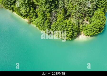 litorale di lago di cava con acqua turchese, e verde foresta a riva. vista aerea dall'alto Foto Stock