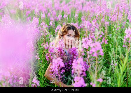 Ritratto esterno di una bella donna bionda di mezza età in un campo con fiori Foto Stock