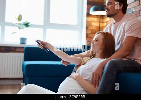 le coppie rilassate hanno tempo libero a casa, l'uomo e la donna sposati giovani che tengono il telecomando, scegliendo un film Foto Stock