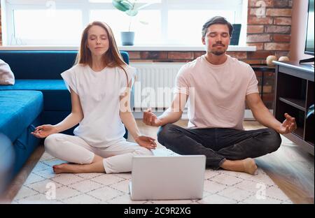 bella coppia caucasica pratica yoga a casa, si siedono in posa di loto, meditate, indossare abbigliamento domestico Foto Stock