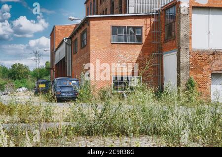 Un vecchio sito industriale abbandonato con un edificio in mattoni rossi con un furgone arrugginito Foto Stock