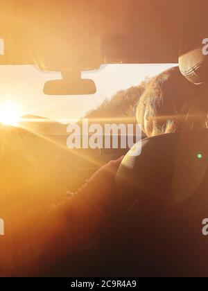 Vista posteriore della donna seduta sul sedile del passeggero in automobile mentre si rilassa durante il viaggio e si gode un tramonto incredibile Foto Stock