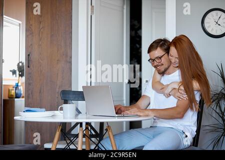 adorabile donna rosso sostegno marito lavorante, giovane donna attenta lo abbraccia, chiede come si sente, è stanco, cosa fare per lui Foto Stock