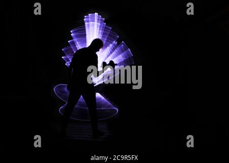 Silhouette di un uomo con manubri. Concetto di bodybuilding ed esercizio fisico. Forma astratta con sciabola luminosa sullo sfondo. Foto Stock