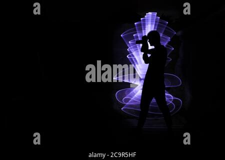 Silhouette di un uomo che fotografa con una fotocamera SLR. Forma astratta con una sciabola di pittura leggera. Foto Stock
