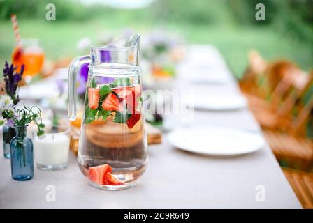 Caraffa di vetro con acqua fresca e menta e fragole poste sul tavolo sulla terrazza per la colazione al mattino Foto Stock