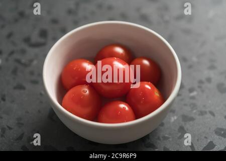 pomodori ciliegini maturi in ciotola bianca su una superficie di cemento Foto Stock