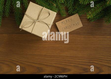 Piatto sfondo di natale con rametti di abete rosso e regalo marrone scatola su superficie di legno di frassino Foto Stock