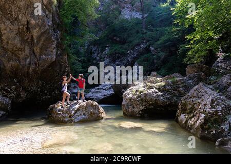 Madre e figlio in piedi su una roccia in un fiume cristallino, dando alto cinque Foto Stock