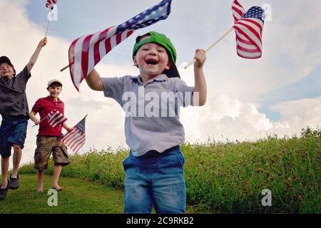 Tre ragazzi che tengono le bandiere americane entusiasticamente mentre agitando loro e. il ragazzo più giovane di fronte è il più felice di tutti con il sorriso più grande Foto Stock