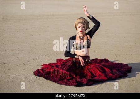 la ragazza di ballerina si siede sulla terra e tiene una mano sulla testa, e la seconda al livello di uno stomaco e gli occhi chiusi in un vestito rosso lungo con Foto Stock