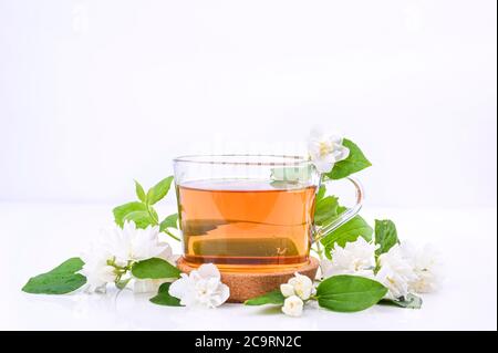 Tè Jasmine. Una bevanda tradizionale in Cina per la salute e la vitalità. Medicina orientale. Fiori freschi di gelsomino su sfondo bianco e una tazza di tè. Spazio libero per il testo. Foto di colori chiari Foto Stock