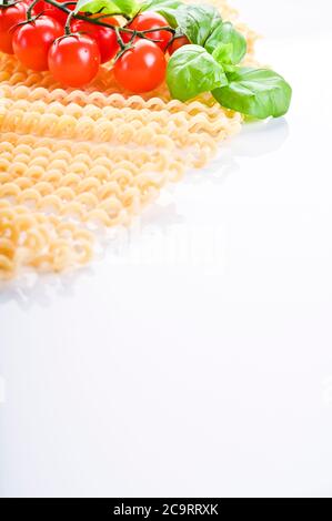 Fusilli lunghi bucati . Pasta lunga riccia su un piatto bianco, con foglie di basilico fresco e pomodori ciliegini. Pasta italiana tradizionale dal sud. Foto di alta qualità. Spazio di copia Foto Stock