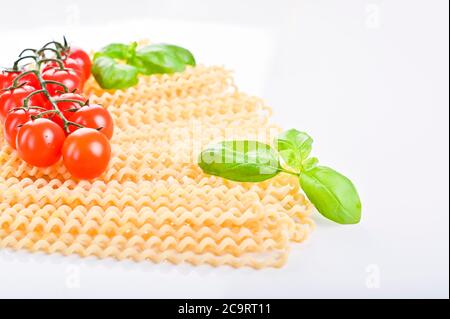 Fusilli lunghi bucati . Pasta lunga riccia su un piatto bianco, con foglie di basilico fresco e pomodori ciliegini. Pasta italiana tradizionale dal sud. Foto di alta qualità. Spazio di copia Foto Stock