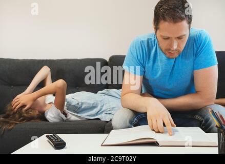 Papà fa i compiti con sua figlia. Legge un libro, ma sua figlia non è interessata. Foto Stock