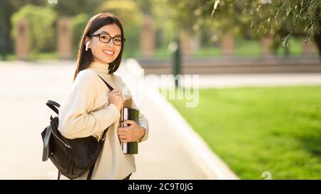 Ragazza in occhiali e cuffie in piedi nel parco Foto Stock