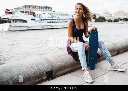 bella donna bionda in posa con uno skateboard in un parco cittadino Foto Stock