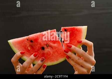 Spezzato grande fetta di anguria matura in mani femminili su sfondo nero, primo piano Foto Stock