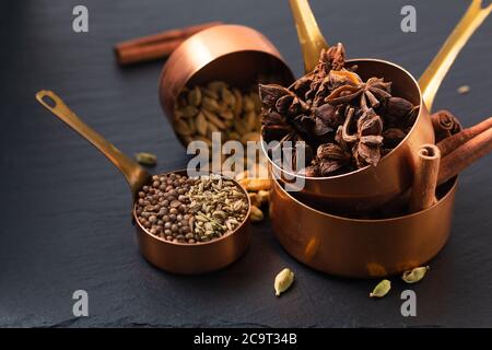 Concetto di cibo miscela di spezie masala, cannella, finocchio, anice stellato, semi di coriandolo e cannella in tazza di rame su tavola di ardesia nera Foto Stock