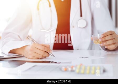 Donna-medico sconosciuto riempie in su la forma di prescrizione in stanza soleggiata, primo piano Foto Stock